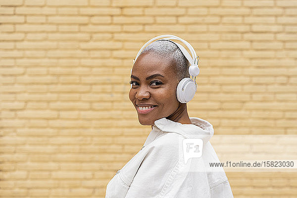 Porträt einer lächelnden Frau  die im Freien mit Kopfhörern Musik hört