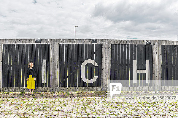 Frau steht vor einem Holzzaun mit Buchstaben