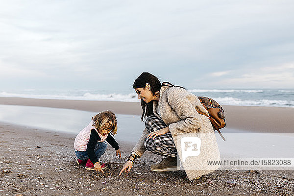 Mutter und Tochter spielen bei Sonnenuntergang am Strand
