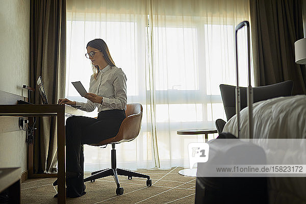 Geschäftsfrau sitzt mit Laptop am Schreibtisch im Hotelzimmer