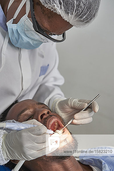 Zahnärztin putzt die Zähne eines Mannes