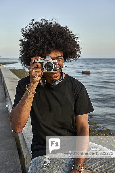 Young man sitting on wall and photographing with his camera at seafront