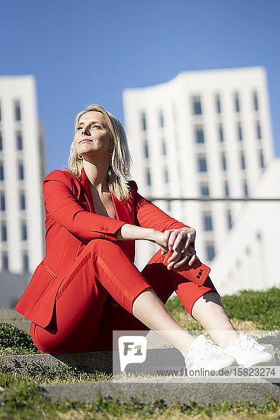 Blonde Geschäftsfrau im roten Anzug  die im Freien auf einer Treppe sitzt