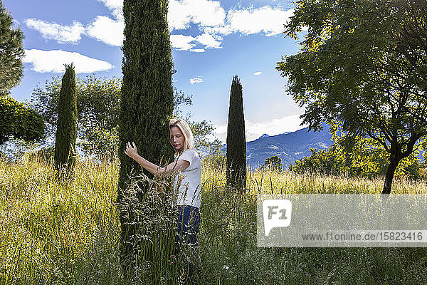 Woman standing in meadow hugging cypresse