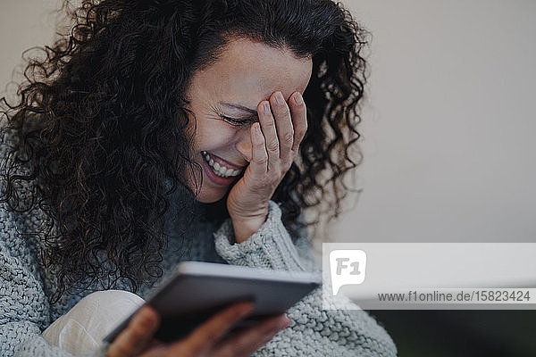 Frau sitzt zu Hause  benutzt digitales Tablet und lacht
