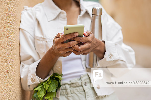 An die Wand gelehnte Frau mit Thermoskanne und Lebensmitteln per Smartphone