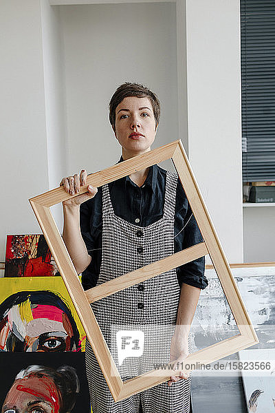 Porträt einer Malerin  die in ihrem Atelier einen Bilderrahmen hält