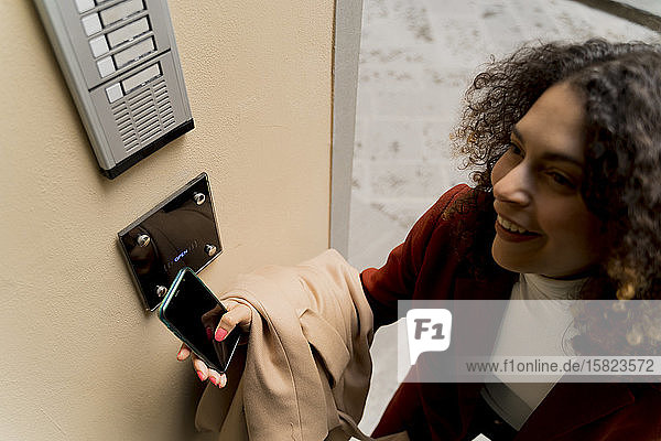 Smiling woman opening door with smartphone