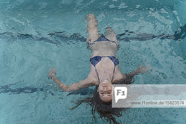 Porträt einer jungen Frau  die im Schwimmbad auf dem Wasser schwimmt