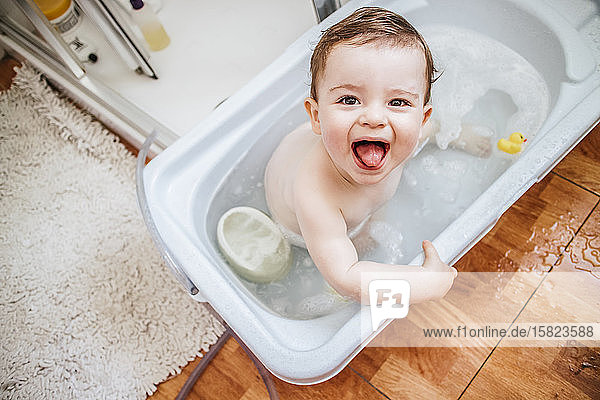 Porträt eines kleinen Jungen in der Badewanne mit herausgestreckter Zunge