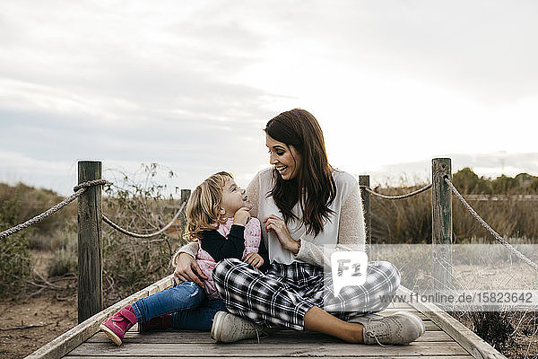 Happy mother and daughter sitting on a boardwalk in the countryside