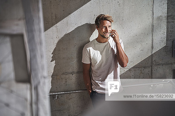 Young man wearing t-shirt talking on the phone at concrete wall