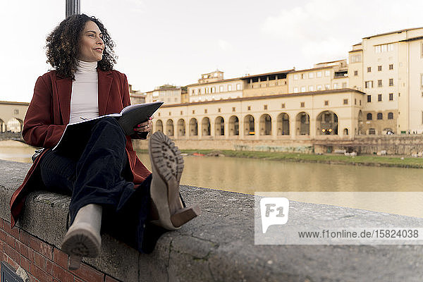 Frau sitzt auf einer Mauer am Arno  Florenz  Italien