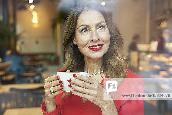 Porträt einer reifen Frau mit einer Tasse Kaffee hinter einer Fensterscheibe