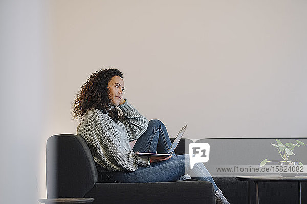 Woman sitting on couch  using laptop  thinking