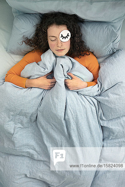 Portrait of sleeping young woman lying in bed with paper mask