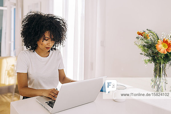 Porträt einer jungen Frau mit lockigem Haar mit Laptop auf dem Tisch zu Hause