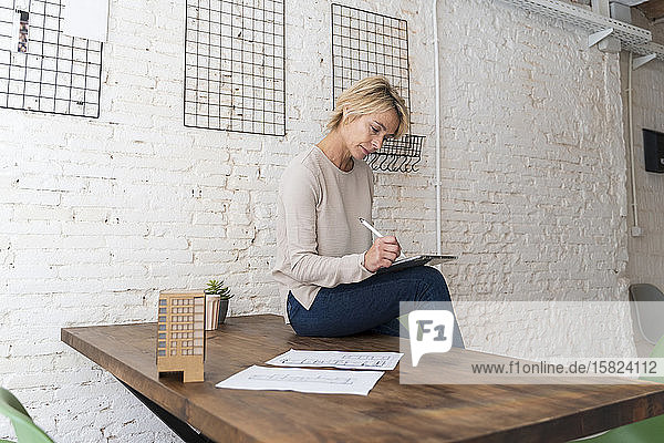 Mature woman at work sitting on desk in architectural office