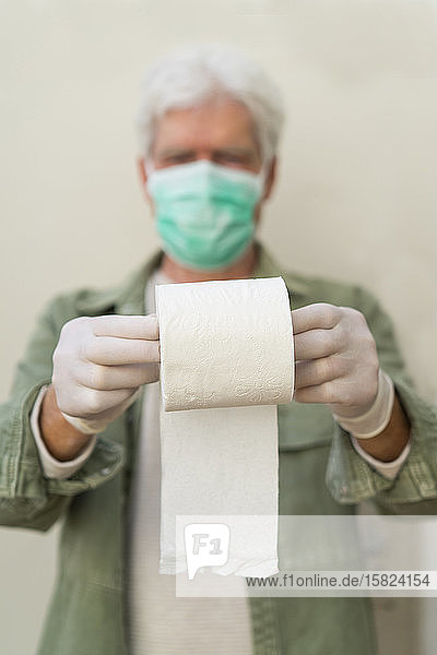 Mann mit Gesichtsmaske und Schutzhandschuhen hält eine Rolle Toilettenpapier