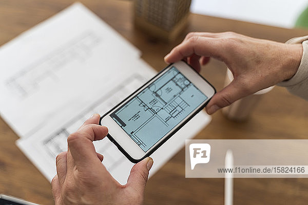 Close-up of woman in architectural office taking cell phone picture of construction plan