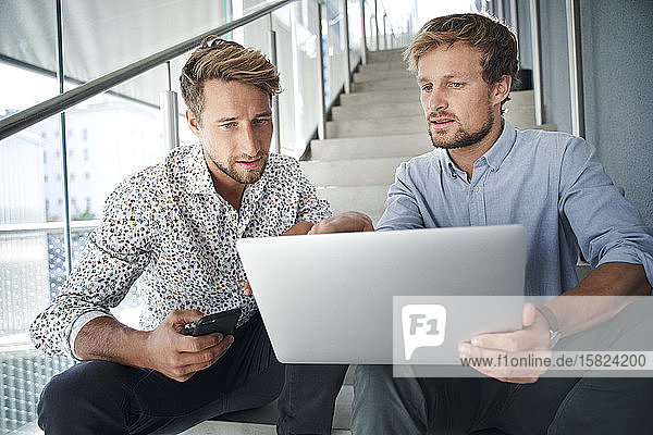 Zwei junge Geschäftsleute sitzen mit Laptop auf der Treppe