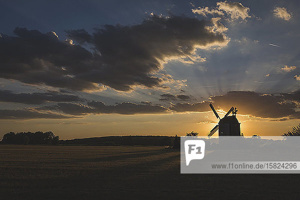 Germany  Brandenburg  Gray clouds over silhouette of countryside windmill at sunset