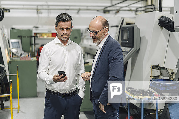 Zwei Geschäftsleute mit Smartphone in einer Fabrik