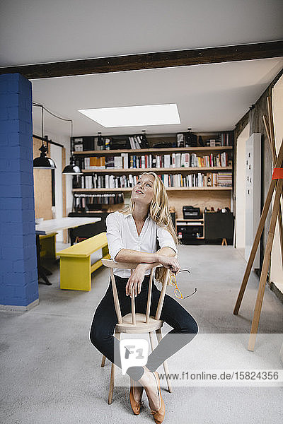 Smiling young businesswoman sitting on a chair in loft office looking up