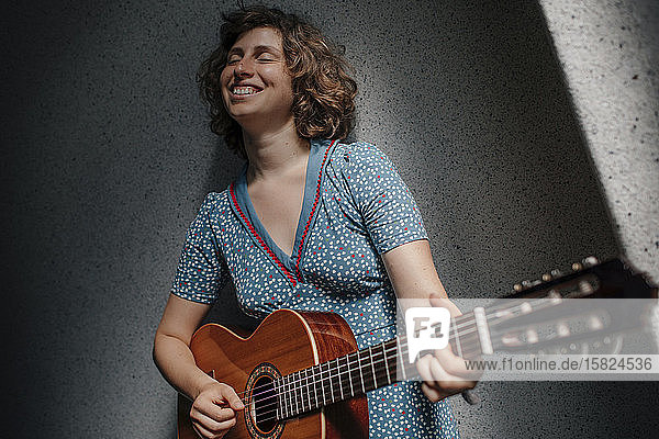 Porträt einer glücklichen jungen Frau  die mit geschlossenen Augen Gitarre spielt