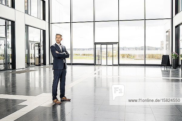 Successful businessman standing in entrance hall of office building  with arms crossed