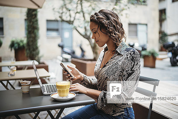 Junge Frau mit Laptop und Smartphone in einem Straßencafé