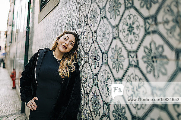 Porträt einer glücklichen  schwarz gekleideten jungen Frau  die an der Azulejo-Wand lehnt  Lissabon  Portugal