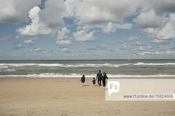 Rückansicht einer Familie mit zwei Kindern  die barfuss am Strand spazieren gehen  Scheveningen  Niederlande