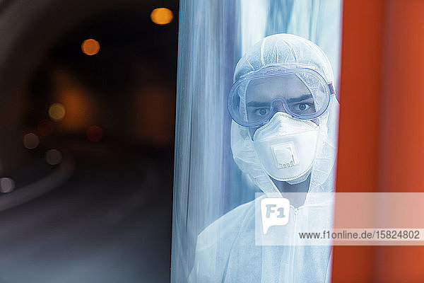 Porträt eines Mannes in Schutzkleidung hinter einer Glasscheibe