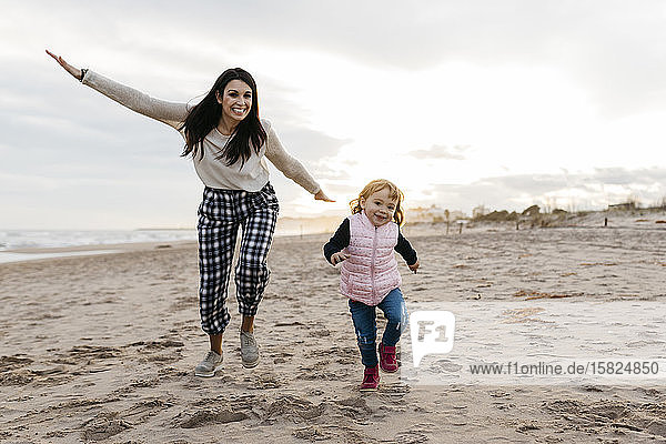 Happy mother and daughter playing on the beach at sunset