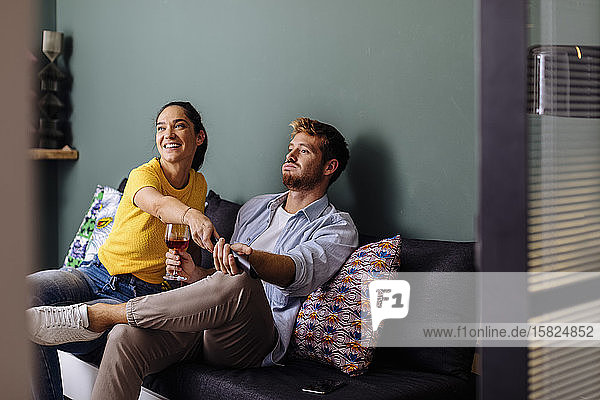 Junges Paar sitzt zu Hause auf der Couch und sieht fern