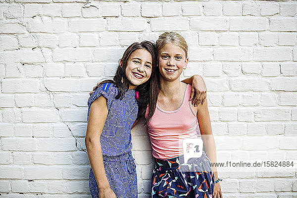 Portrait of two happy girls embracing at a wall