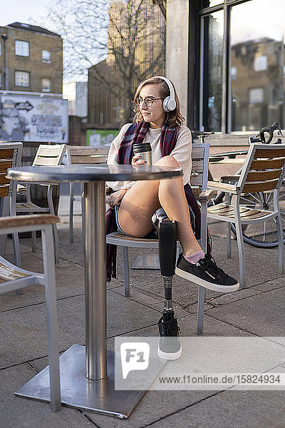 Young woman with leg prosthesis sitting in a sidewalk cafe in the city