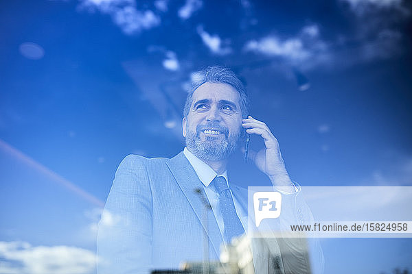 Portrait of a mature businessman on the phone behind windowpane