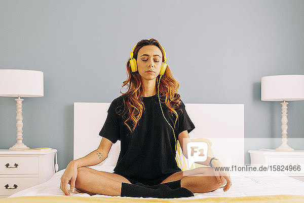 Junge Frau meditiert zu Hause mit Kopfhörern am Bett