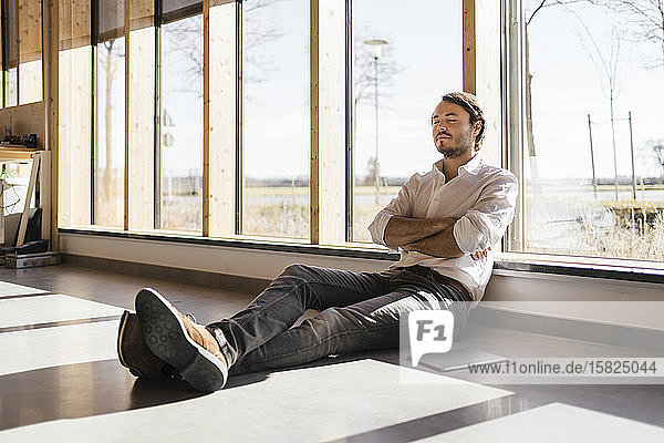 Businessman with closed eyes sitting at the window in open-plan office