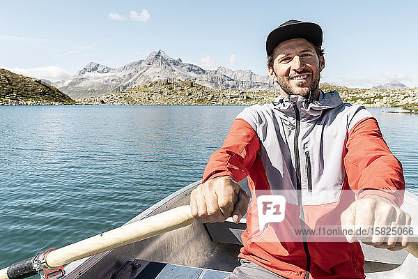 Junger lächelnder Mann in einem Ruderboot  Suretta-See  Graubünden  Schweiz