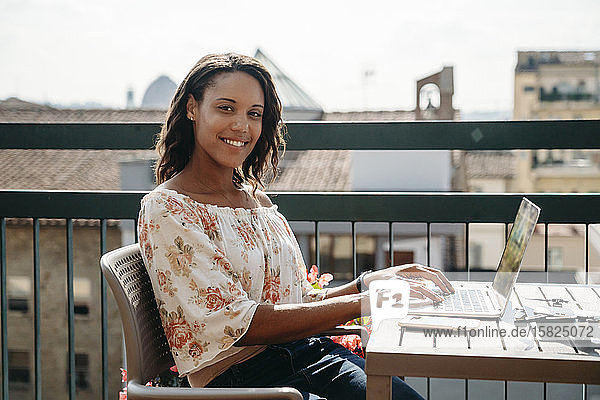 Portrait of smiling young woman using laptop on a balcony in Florence  Italy