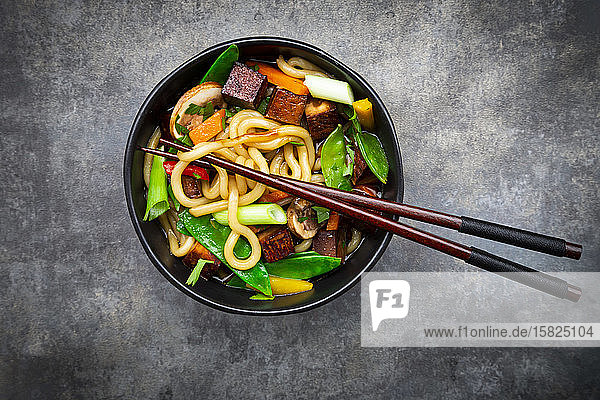 Ein Paar Stäbchen und eine Schüssel fertige Misosuppe mit Udon-Nudeln  Tofu  Zuckerschoten  Paprika  Karotten  Mu-err-Pilzen  Frühlingszwiebeln und Koriander