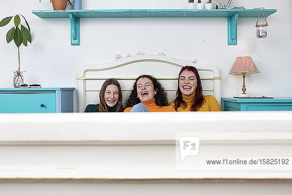 Portrait of three laughing sisters sitting side by side on bed