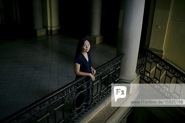 Porträt einer ernsten Frau  die in einem alten Gebäude am Geländer lehnt und in die Ferne schaut