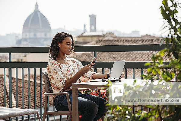 Junge Frau mit Laptop und Smartphone auf einem Balkon in Florenz  Italien