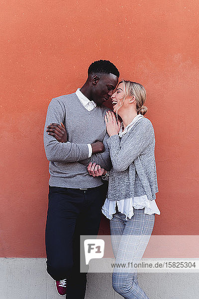 Glückliches  liebevolles junges Paar steht an einer orangefarbenen Wand