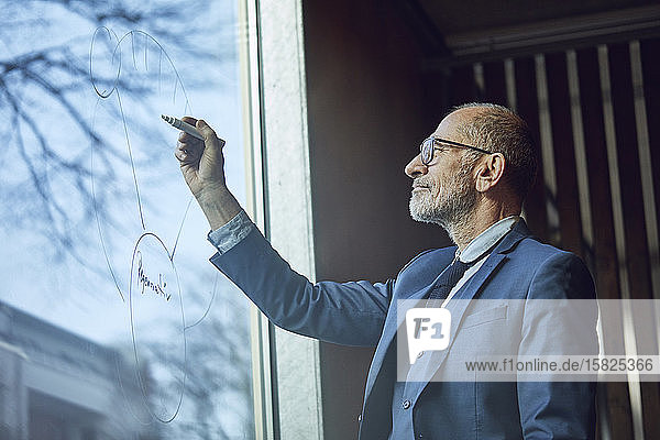 Leitender Geschäftsmann zeichnet Diagramm auf Fensterscheibe