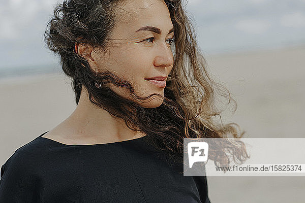 Porträt einer lächelnden Frau mit wehendem Haar am Strand
